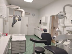 Wnętrze gabinetu stomatologicznego z fotelem dentystycznym i sprzętem medycznym.