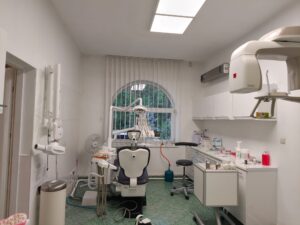Wnętrze gabinetu stomatologicznego z fotelem dentystycznym i sprzętem medycznym.