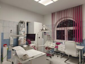 Wnętrze gabinetu stomatologicznego z fotelem dentystycznym i sprzętem medycznym.