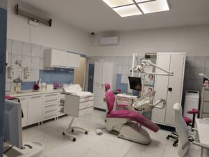 Wnętrze gabinetu stomatologicznego z fotelem dentystycznym i sprzętem medycznym.